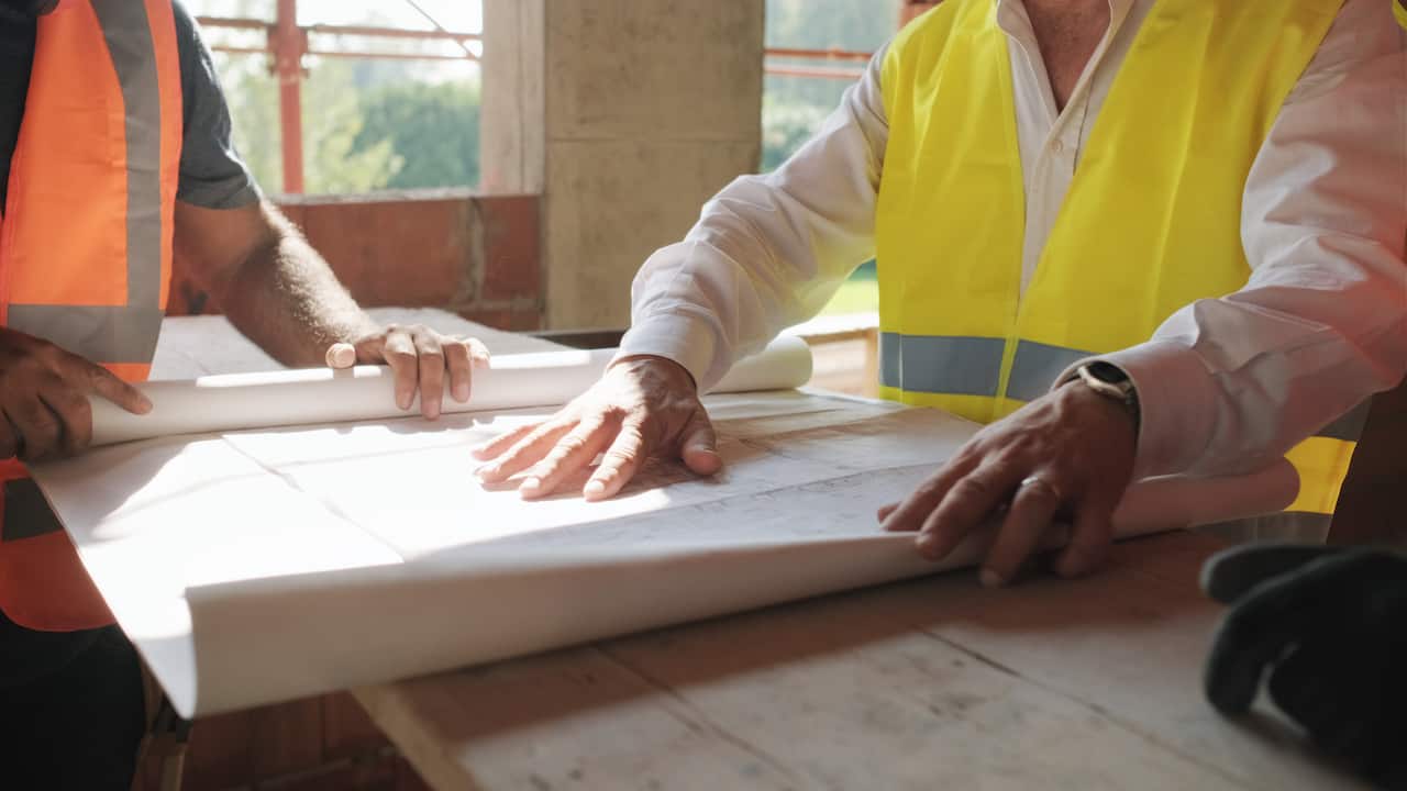 People working in construction site. Men at work in new housing project. Team of workers at work talking with supervisor and looking at plans